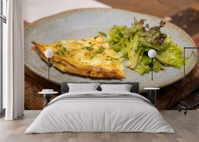 A slice of Cheesy Macaroni and Vegetable Frittata Bake on a grey plate placed on a wooden kitchen table Wall mural