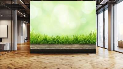 A fresh spring sunny garden background of green grass and blurred foliage bokeh with a wooden table to place cut out products on. Wall mural