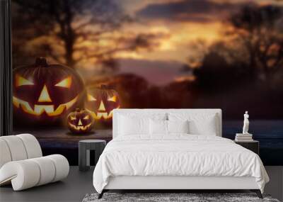 A spooky forest sunset with a haunted evil glowing eyes of Jack O' Lanterns on the left of a wooden bench on a scary halloween night. Wall mural