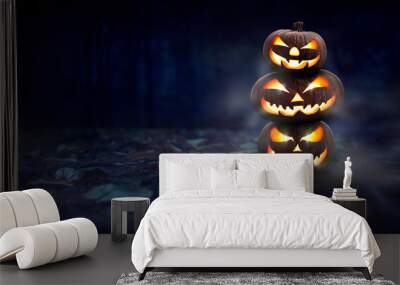 A stack of 3 spooky halloween pumpkin, Jack O Lantern, with an evil face and eyes on the forest floor at night with a dark background. Wall mural