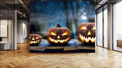 Three spooky halloween pumpkins in a row, Jack O Lantern, with evil face and eyes on a wooden bench, table with a misty night forest background Wall mural