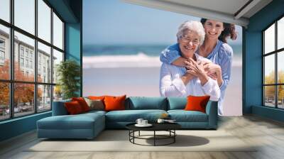 Portrait, beach and young woman with her senior mother embrace and smile together outdoors on mockup. Family, happy and hugging elderly lady with adult daughter or at the ocean or sea for travel Wall mural