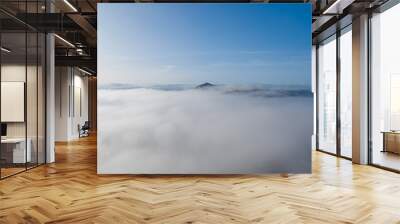 Mountain sitting above the clouds with blue skies and thick fog Wall mural