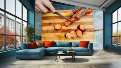 Close up of man hands cutting bbq sausage with knife Wall mural