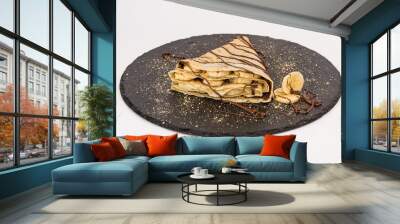 Homemade folded crepe with chocolate cream and banana slices on black round plate isolated on white background Wall mural