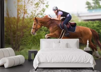 Young pretty girl riding a horse with backlit leaves behind in spring time Wall mural