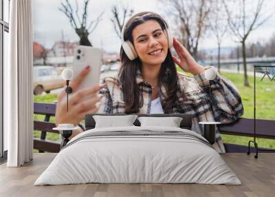 One young girl is listening to music on her wireless headphones and using her phone outdoors on a sunny day	 Wall mural