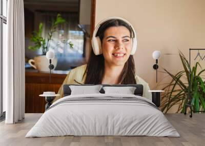 One young girl or woman is listening to music on her wireless headphones while drinking her morning coffee or tea in the house before going to work Wall mural