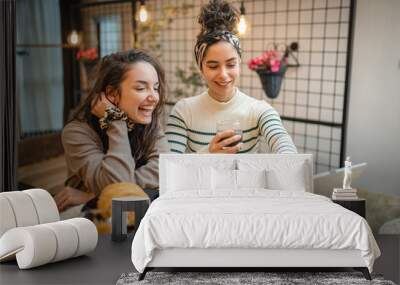 Two friends or girlfriends or sisters are eating croissant and drinking coffee for breakfast while watching something on tablet in their apartment  Wall mural