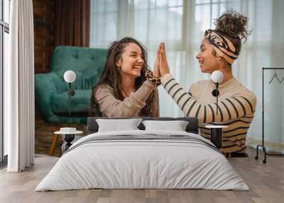 Two friends or girlfriends or sisters are high fiving and smiling because they made good purchase online while using credit card on their laptop in their apartment  Wall mural