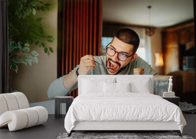 Young caucasian man eating corn flakes for breakfast at home Wall mural