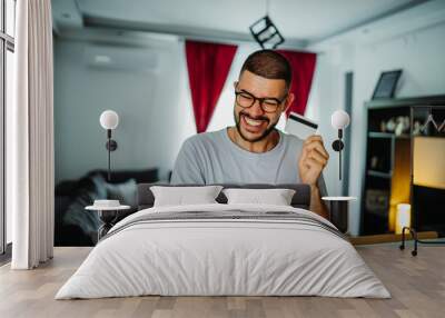 Young caucasian man shopping online on mobile phone using credit card Wall mural