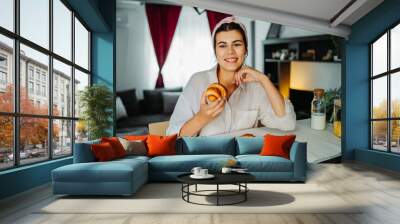 Young caucasian woman eating croissant for breakfast Wall mural