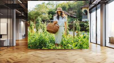 Young caucasian woman harvesting peppers in home garden with basket Wall mural