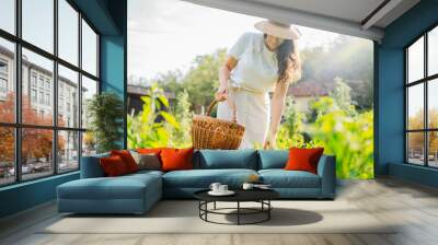 Young caucasian woman harvesting peppers in home garden with basket
 Wall mural