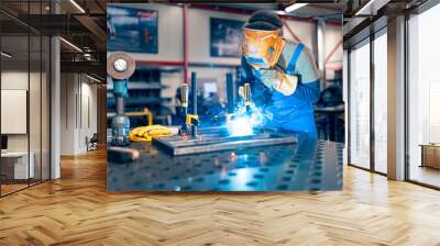 A worker is using a welding machine in his hand and working on a metal rod, he is wearing his visor for protection Wall mural