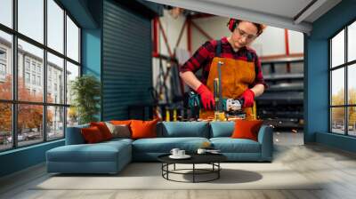 A young girl who is an apprentice in a metal workshop uses a grinder and works on a metal bar, she is wearing protective equipment Wall mural