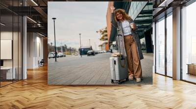 After the flight, a curly-haired redhead outside the airport raises her hand, signaling for a taxi with her suitcase. Wall mural