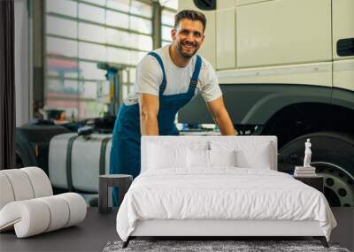 Portrait of positive smiling truck serviceman with tools standing by truck vehicle in workshop. Truck vehicle maintenance and servicing. Wall mural