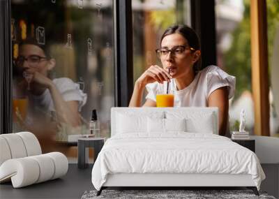 A college girl is sitting in a bar, sipping fresh orange juice on a break between lectures. A healthy way to kill time. A girl in a bar drinking juice Wall mural