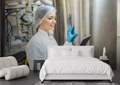 A dairy factory worker is checking on milk processing machine and smiling at the tablet. Wall mural