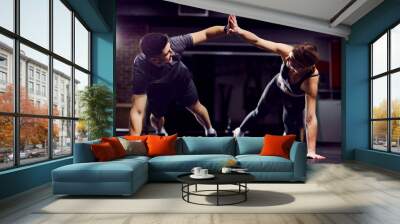 A fit sporty couple giving high five to each other while doing planks and exercises in a gym. Wall mural