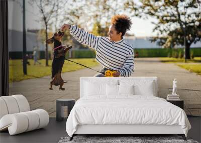 A girl is playing with her pet while he is jumping and eating treats outdoors. Wall mural