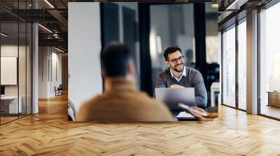 A happy businessman is sitting in the co working space with colleagues and having briefing. Wall mural