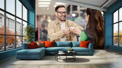 A happy man giving credit card to cashier in supermarket and paying check. Wall mural