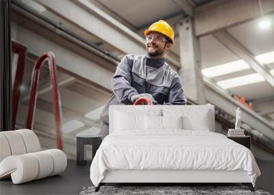 A smiling factory supervisor in a protective uniform stands on the height and monitors work in a factory. Wall mural