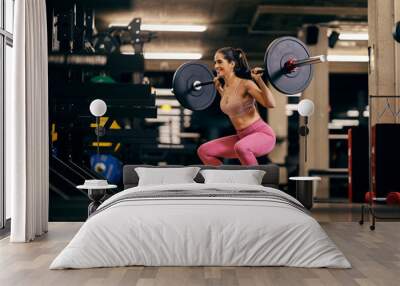 A sportswoman is doing squats while lifting barbell in a gym. Wall mural