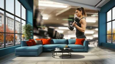 A strong sportswoman is exercising with dumbbell in a gym. Wall mural