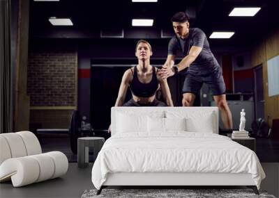 A young strong sportswoman lifting weights in gym with her personal trainer. Wall mural