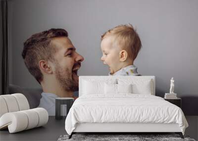 Adorable little blond boy playing with his caring father and biting his nose. Father is smiling. Wall mural