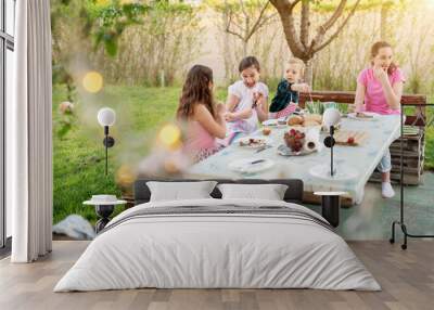 After they finished meat from the stick, two playful girls are poking each other with sticks while their older sister and toddler brother are eating. Wall mural