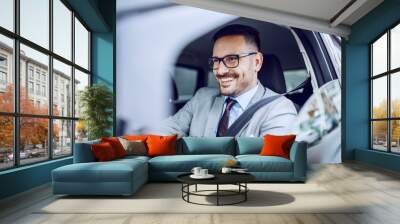 Attractive caucasian smiling elegant unshaven businessman in suit and eyeglasses driving his expensive car. Wall mural