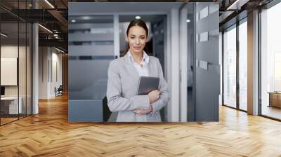 Beautiful positive Caucasian businesswoman in formal wear standing in hall and holding tablet. Wall mural