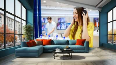 Close up of adorable attractive happy girl testing headphones in a tech store. Wall mural