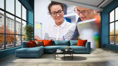 Close up of two charming satisfied professional women sitting in the office and working together one next to another. Wall mural