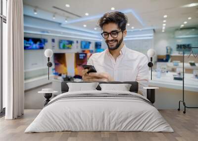 Close up portrait view of satisfied excited happy smiling young student bearded man with eyeglasses looking at mobile in a tech store. Wall mural