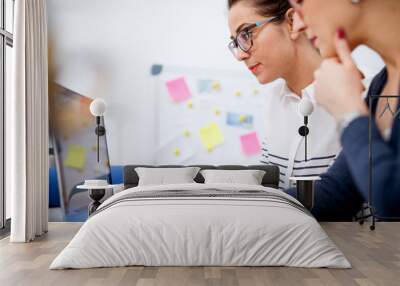 Close up side view of two focused professional productive women sitting in the office and working together one next to another on a laptop. Wall mural