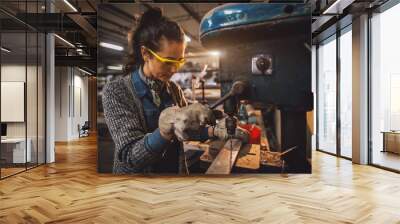 Close up view of hardworking attractive professional serious woman working with an electric drill in the fabric workshop. Wall mural