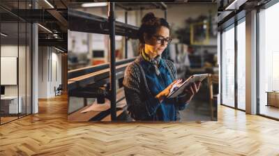 Close up view of hardworking focused professional motivated business woman holding a tablet next to the shelf with metal pipes in the fabric workshop. Wall mural