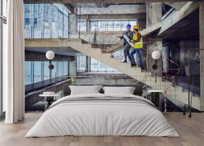 Construction worker and main architect climbing the stairs and talking about progress in construction of new building. Wall mural