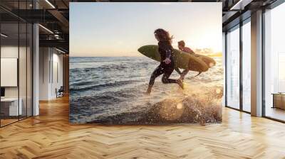 Couple is running into the water with surfboards. Wall mural