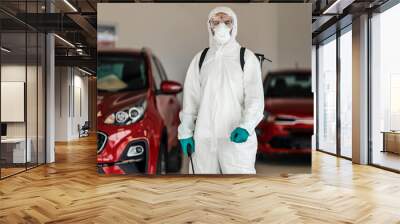 COVID-19 danger alert, stop spreading a virus. A male professional in a protective suit prevents the spread of the infection in the auto salon. Coronavirus defense, stay healthy, warning for COVID 19 Wall mural