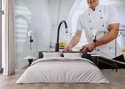 Cropped picture of caucasian chef in uniform washing kitchen knife in sink. Kitchen interior. Wall mural