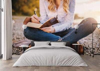 Cropped picture of focused fashionable beautiful caucasian woman sitting near river and holding notebook. Wall mural