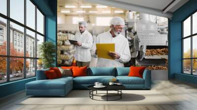 Father and son walking through their food factory in sterile clothes . Taking notes about food quality and looking satisfied. Wall mural