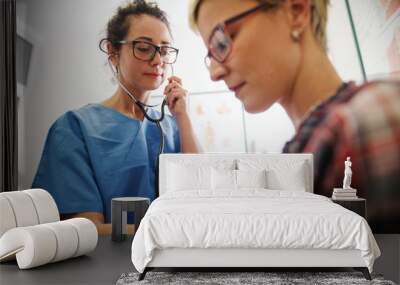 Female middle-aged doctor using stethoscope to examine patient. Wall mural